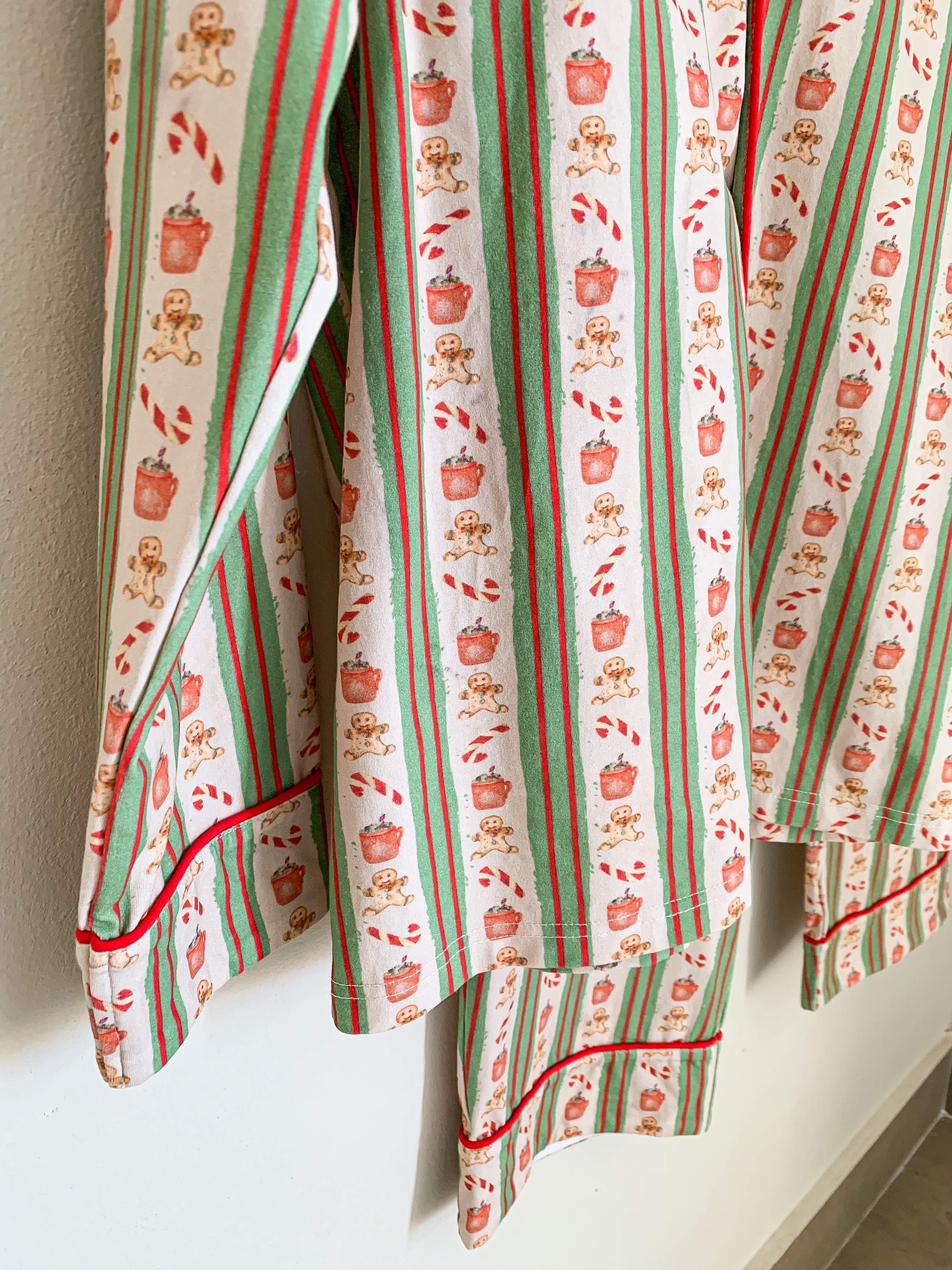 close up image of adult Christmas pjs. it shows the bottom part of the pants and also the arm of the top. the pattern is red and green with beige stripes that are patterned with Christmas icons like gingerbread.