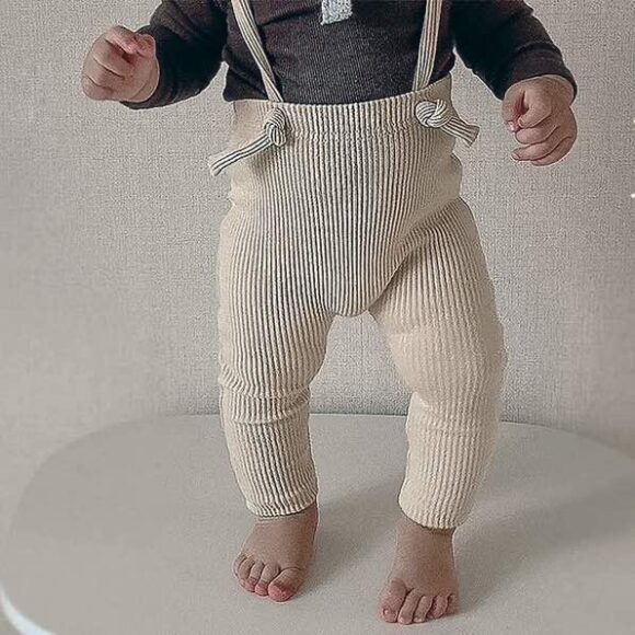 Baby wearing cream colour stretchy rib cotton suspenders, standing up.