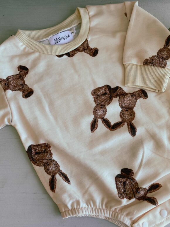 organic cotton romper laid down on a plain surface for show. the bunny rabbit pattern is on show, brown bunny on beige background.