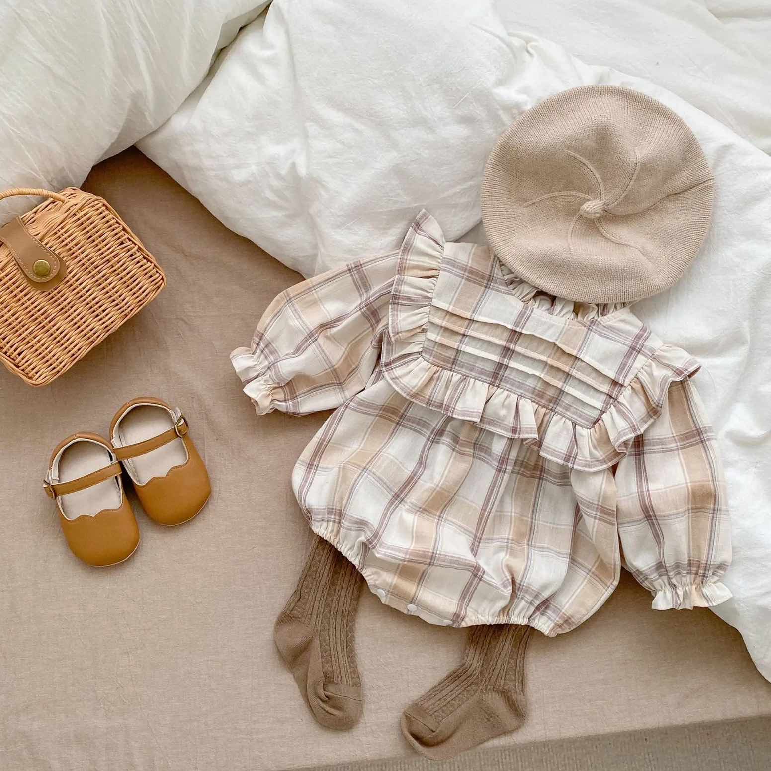 frilly romper displayed with baby socks, beret, rattan bag and baby shoes.
