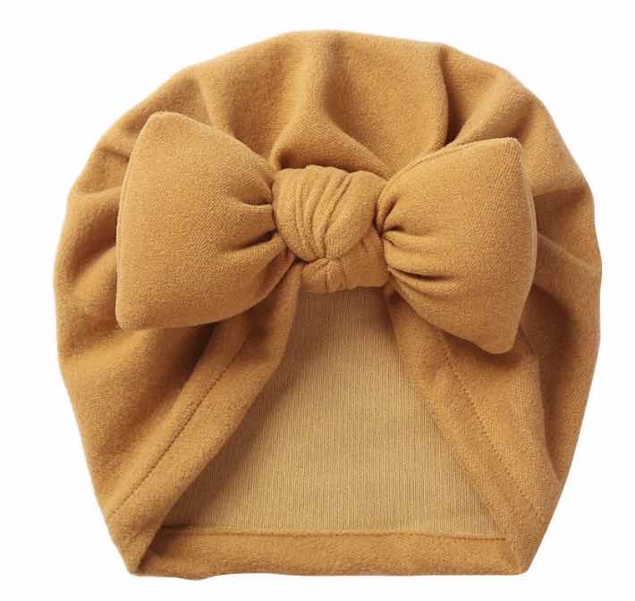 mustard colour baby turban. Displayed on a white background highlighting size of bow at the front of the hat.