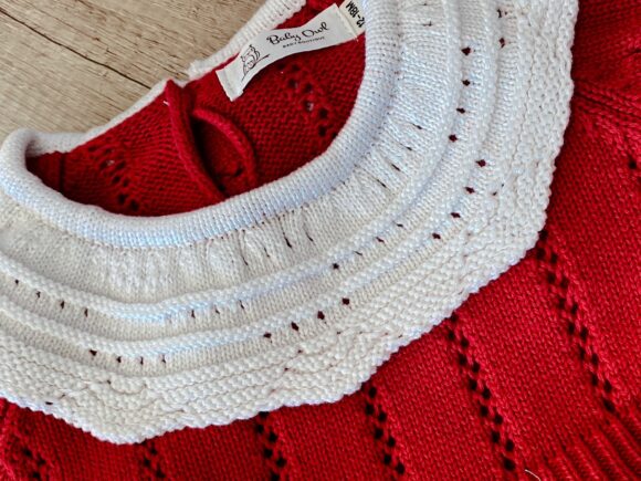 up close picture of a knitted red Christmas romper. the close up picture shows the detail in the stitching and the white fancy frilly collar.