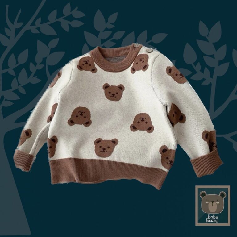 Ecru and brown sweatshirt with teddy bear print is displayed one a navy blue background. It is laid flat to highlight the shape of the jumper. It has a rounded shape and contrast brown trim at the bottom of the body and long sleeves.