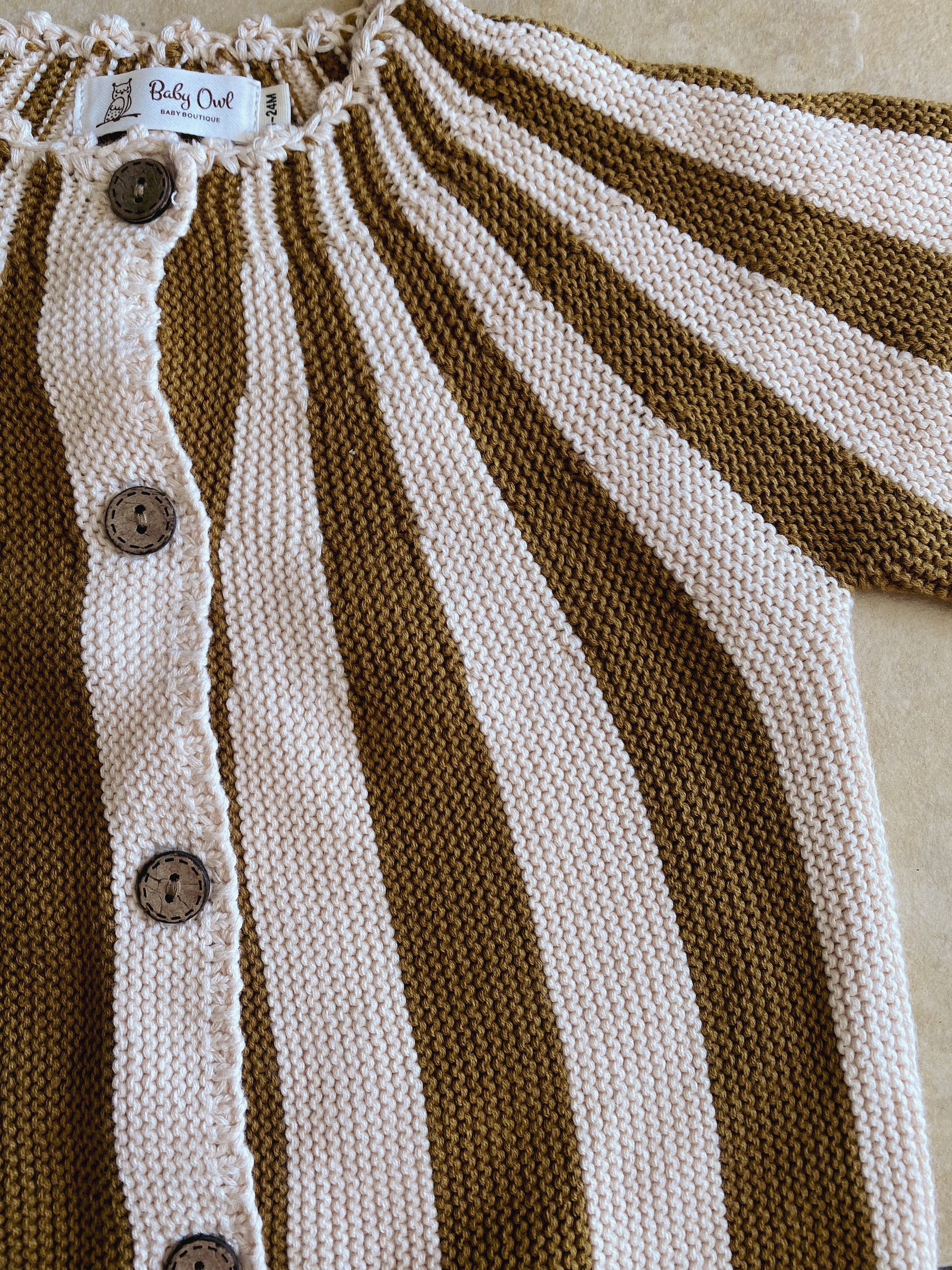 Close up of a knitted girls cardigan. Caramel and beige striped. Wooden buttons at front.