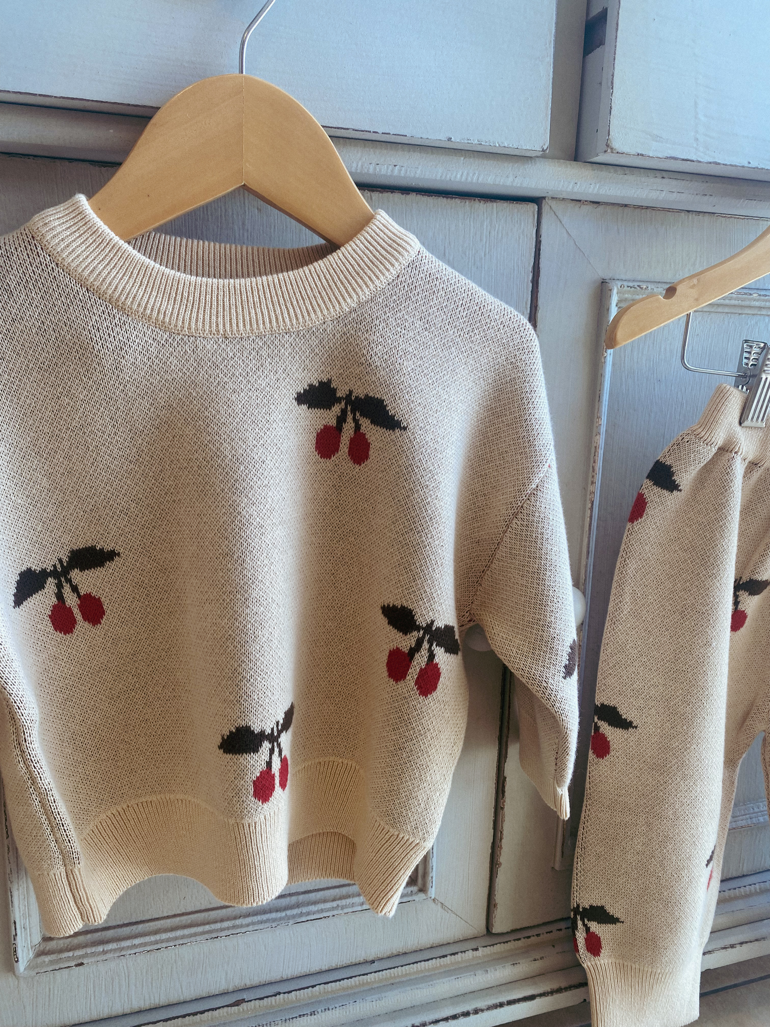 cream colour knitted sweatshirt with cherry print on it. close up picture shoes the top hanging from a wooden hanger.