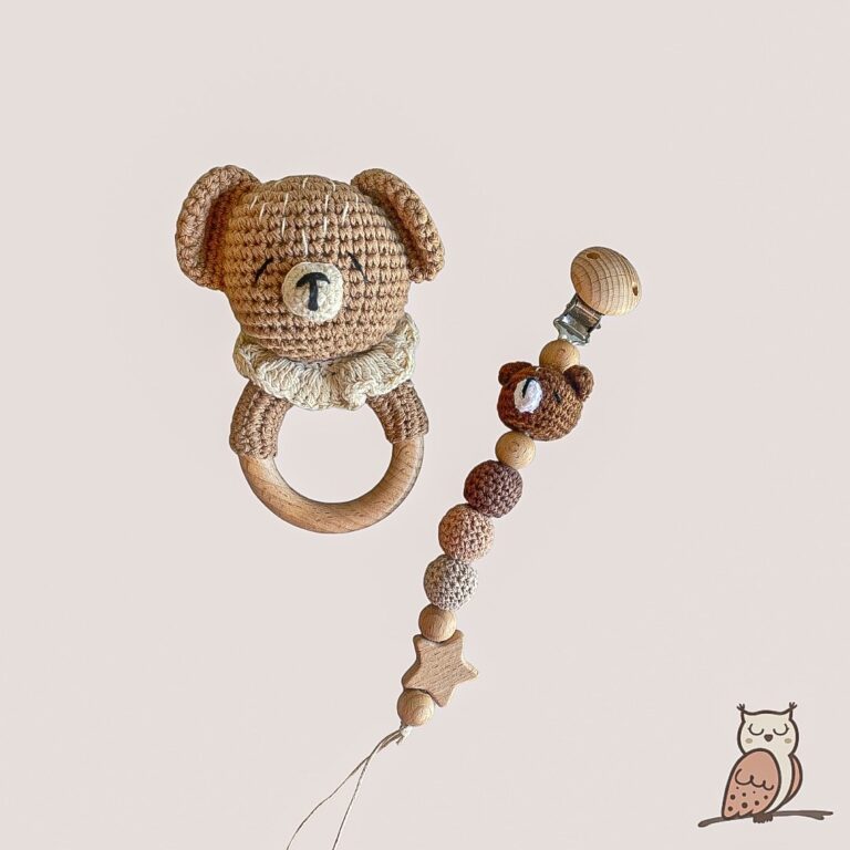 knitted crochet bear rattle and pacifier clip gift set. The knitted rattle has a light brown bear head and is sewn onto a beech wood ring. The pacifier clip has a brown bear head and three balls, 2 knitted crochet and one beech wood, plus one beech wood clip and star.