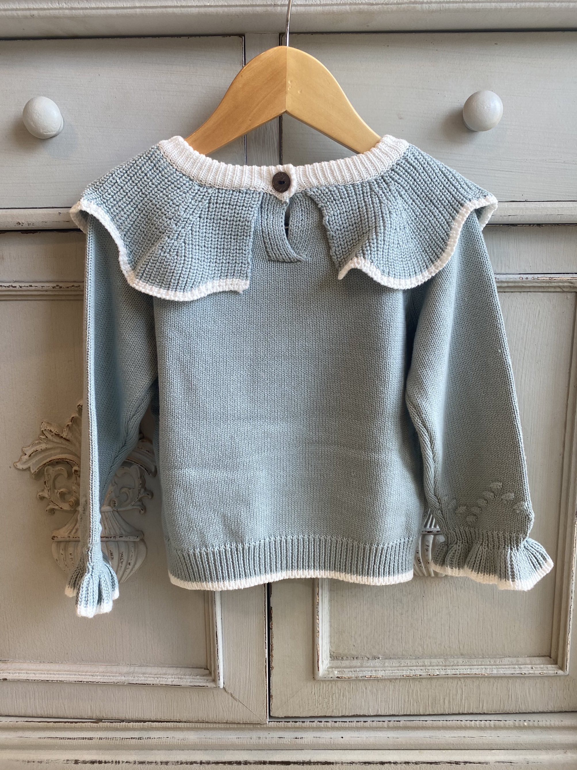 the back of a blue knitted winter toddler girls jumper. Retro style;e with white trim and frilly collar and cuffs.